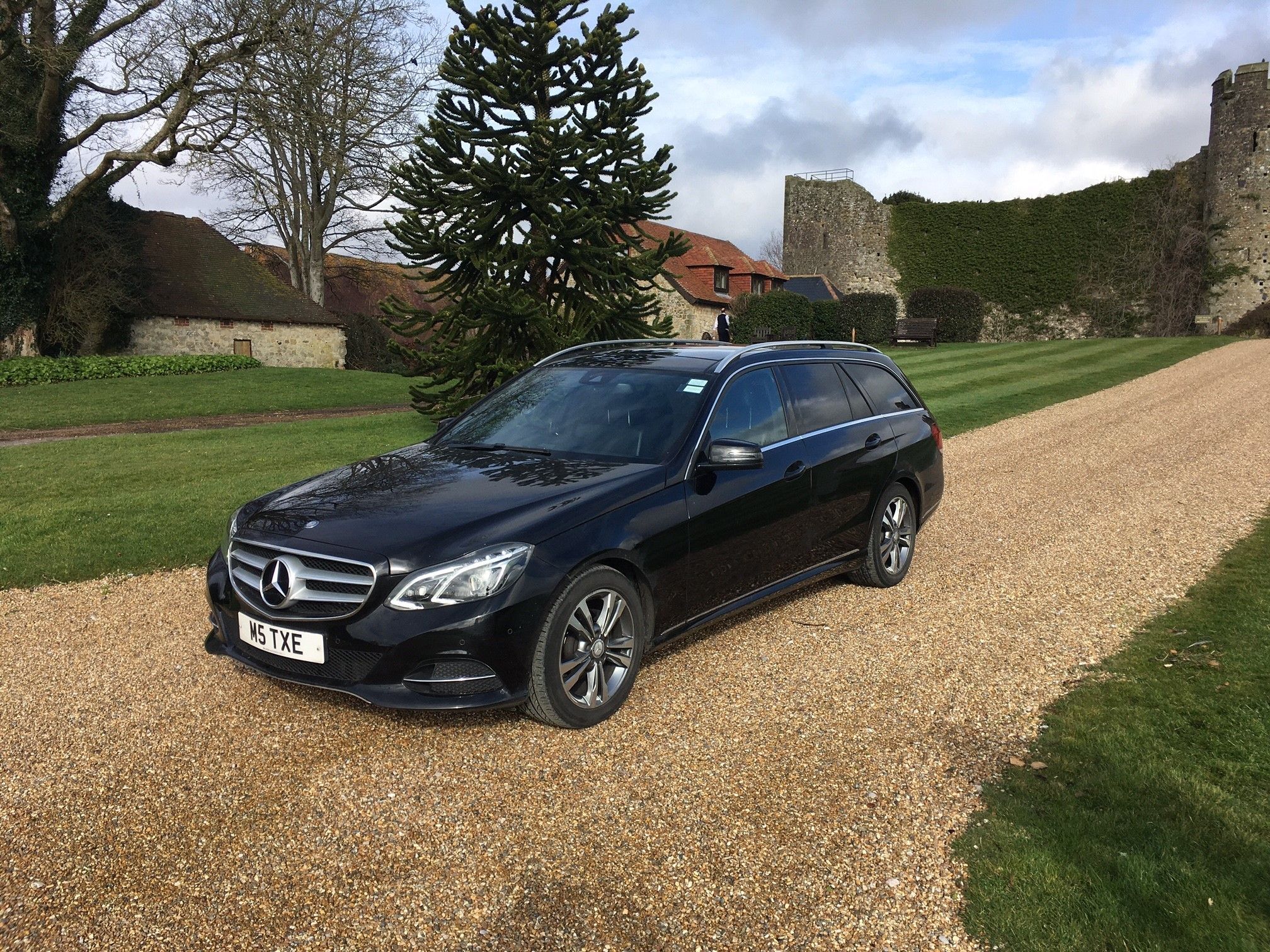 Black Mercedes-Benz E-Class estate on a gravel drive beside a striped lawn