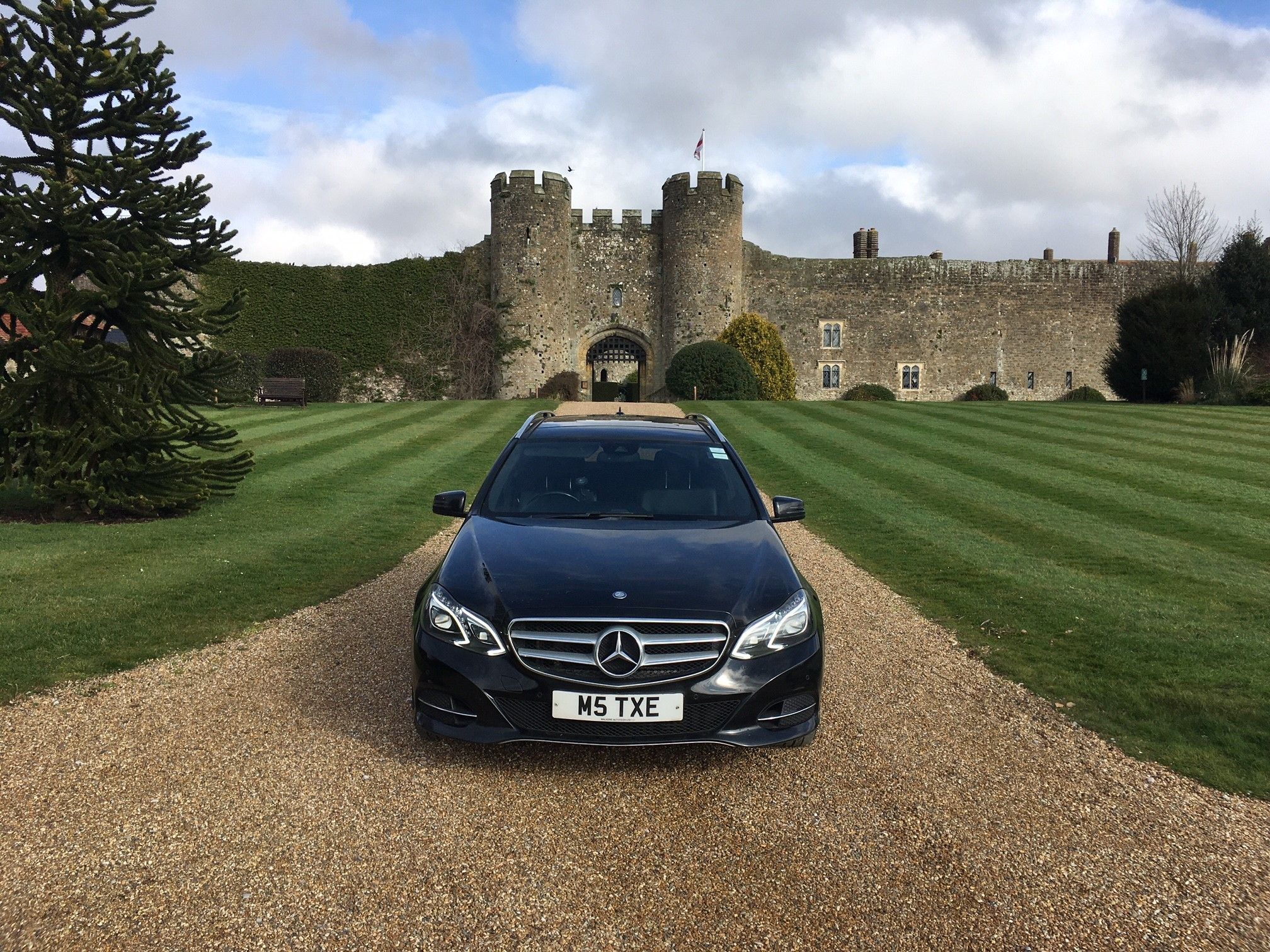 Black Mercedes-Benz E-Class estate on the drive of a castle, lawns striped either side