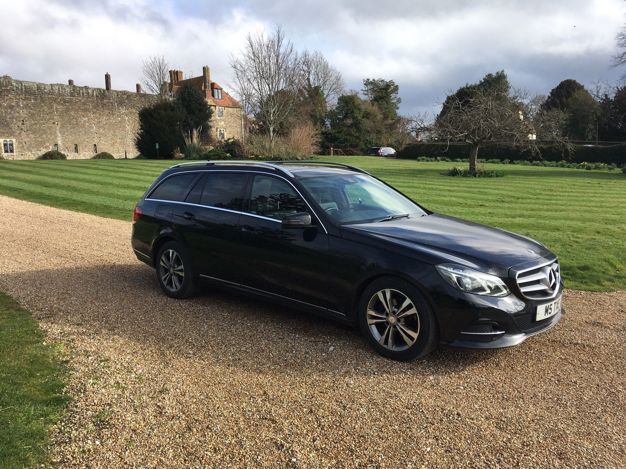 Black Mercedes-Benz E-Class estate side-on, castle walls behind